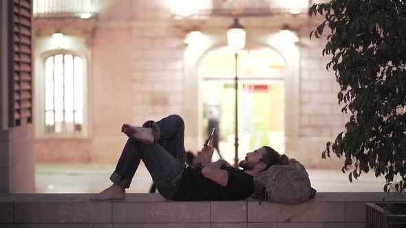 Backpacker with Dirty Feet Scrolling Through Phone Looks and Smiles for the Camera