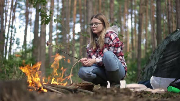 Young Woman on Hunkers Frying Mushroom on Bonfire in Forest