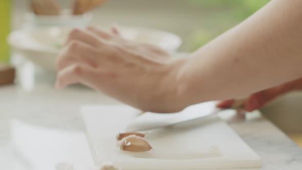 Woman crushing garlic on wooden board in kitchen