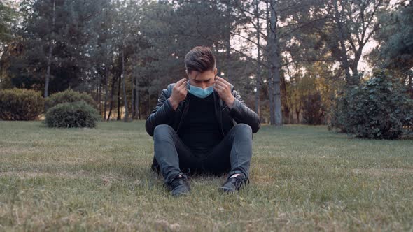 An Adult Is Sitting on the Grass. There Are Trees in the Back That Have Turned Green.