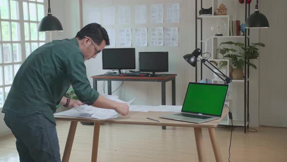 Creative Designer Works On A Storyboard, Looks At His Sketches With Mock Up Green Screen Laptop