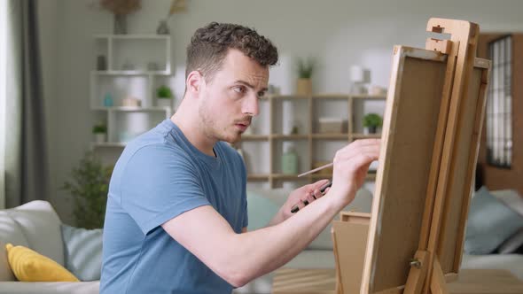 Young Man is Working in His Modern Home Studio in the Morning Drawing on Canvas Enjoying the Process