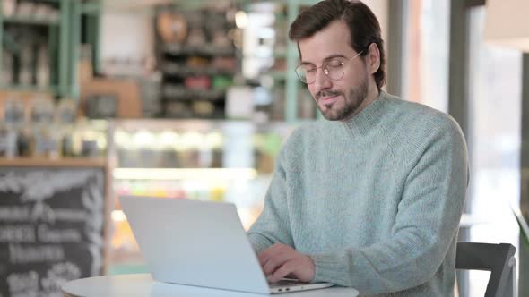 Thumbs Up By Young Man with Laptop in Cafe