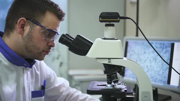 Male Lab Tech Doctor Scientist Looking Into Microscope Connected to Computer Monitor Spbd