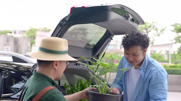 4K Asian man plant shop owner helping customer put potted plants in car trunk.