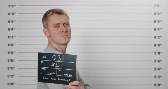 Side Profile Mugshot of Man Holding Sign While Being Photographed in Police Department