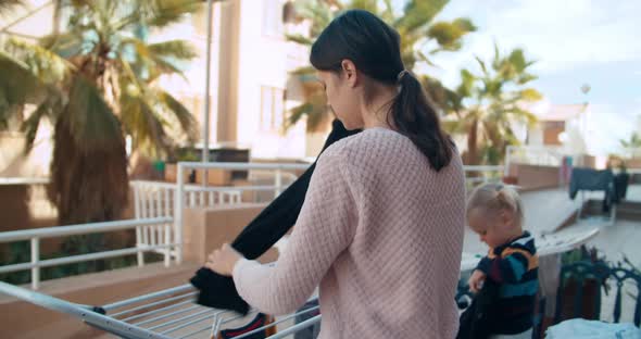 Young woman with daughter baby girl hanging up wet laundry outdoors