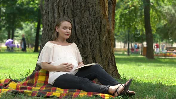 Pregnant Woman Reading Book in Park, Relaxing Outdoors, Health and Prenatal Care