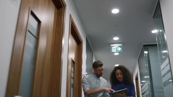 Multiracial Business Team Talking Finance Plan Using Tablet in Office Hallway