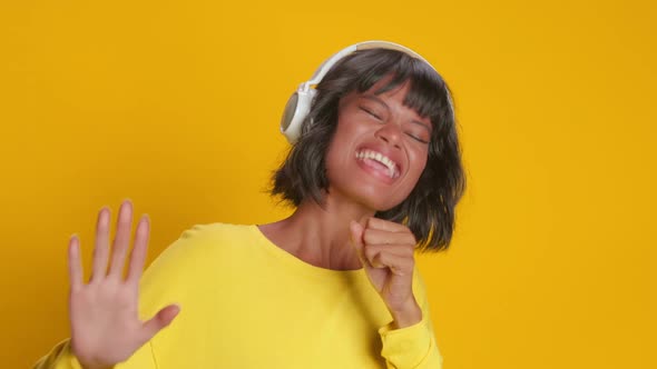 Joyful Woman Listens Pleasant Music in Headphones and Against Yellow Background