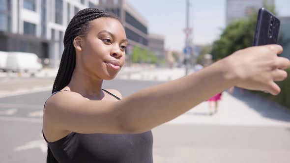 A Young Black Woman Takes Selfies with a Smartphone - a Townscape in the Blurry Background