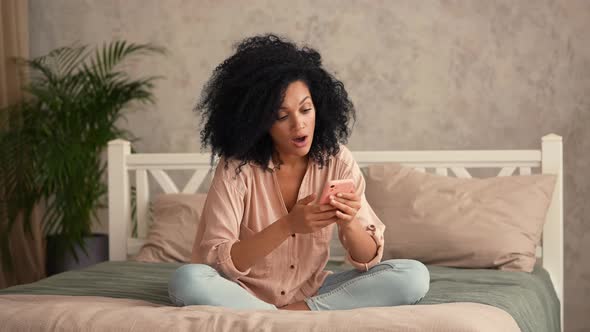 African American Woman Looks Information on Mobile Phone Happily Celebrates Victory Received Good