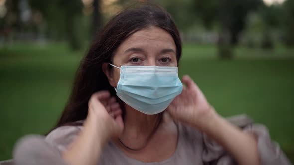 Closeup Portrait of Serious Senior Caucasian Woman Putting on Coronavirus Face Mask Looking at