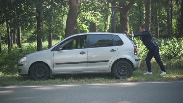 Wide Shot Man Pushing Broken Car with Breakdown Lights on on Suburban Roadside