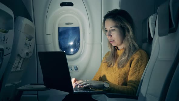 Plane Cabin at Night with a Woman Operating a Laptop