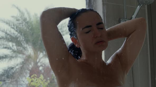 Backside View of Woman in Swimsuit Takes Rain Shower Tropical Greenery on Background