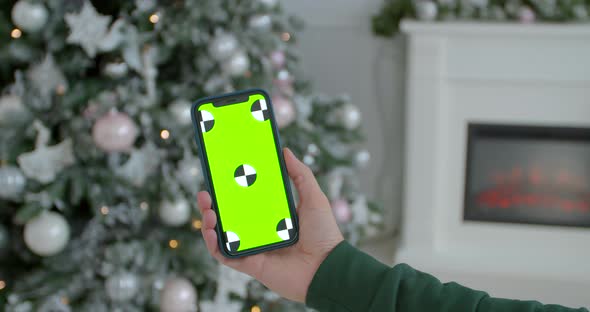 Man Holding a Mock-up Smartphone Greenscreen Chrome Key in New Year Decorated Room. Closeup of Male