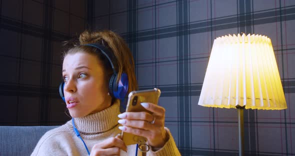 A 30Yearold Woman in Headphones Listening to the Music Singing and Online Messaging Via Smartphone