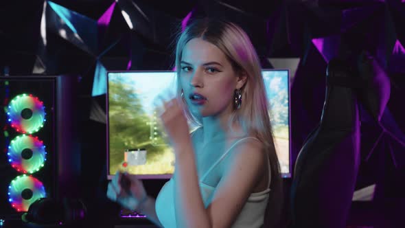 Young Blonde Woman Sitting in Neon Gaming Club  Turning Away From the PC and Looking in the Camera