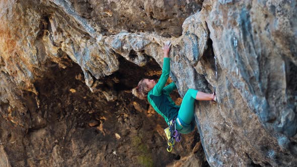 Strong Woman Rock Climber Climbs Hard Tough Rock Route on Very Overhanging Black Cliff in Cave