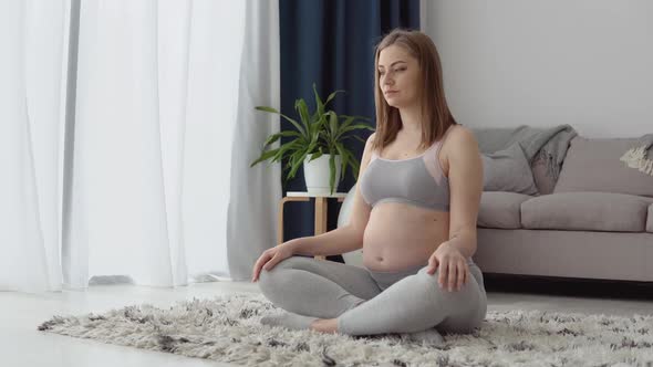 Pregnant Woman in Sportswear Sitting on the Carpet in the Lotus Position