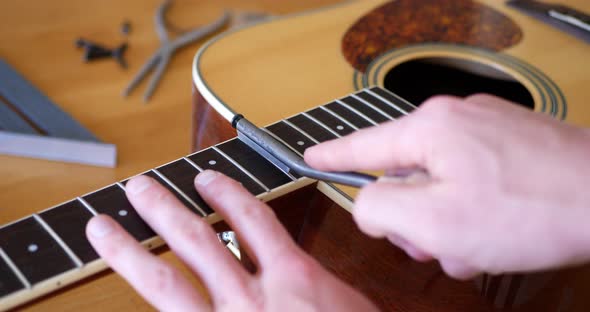 Close up hands of a luthier filing and crowning the frets of an acoustic guitar neck fretboard on a