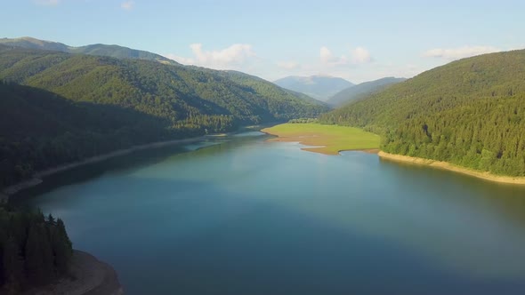 Aerial view of big lake with clear blue water between high mountain hills covered with dense