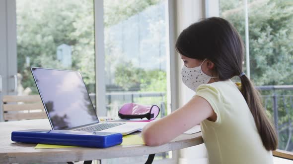 Girl wearing face mask using laptop at home