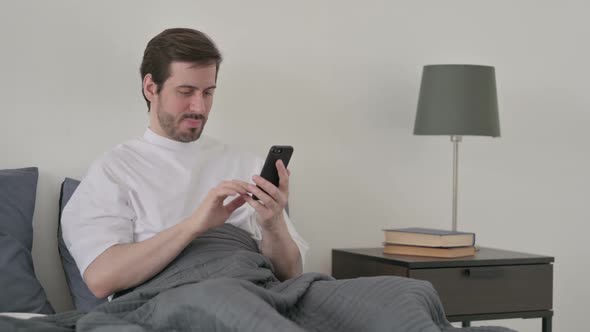 Young Man Reacting to Loss on Smartphone in Bed