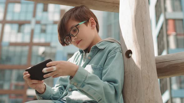 Caucasian Boy Playing Games on Smartphone Outdoors