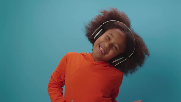 7 years old black girl in headphones dancing and singing looking at camera on blue background