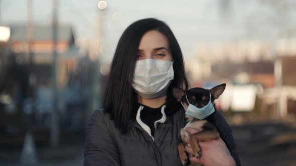 Woman in Protective Face Mask with Small Dog Wearing Medical Mask Too