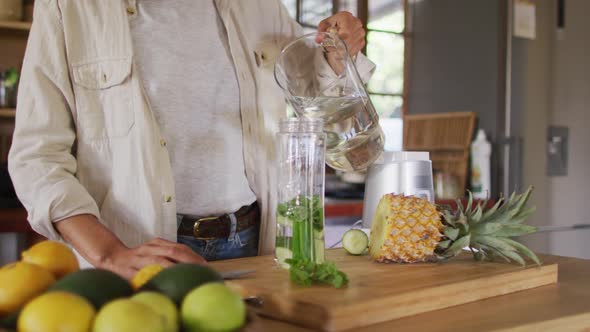 Midsection of mixed race woman preparing health drink standing at counter in cottage kitchen