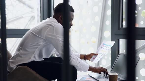 African American Manager Entering Datas from Report with Charts to the Computer