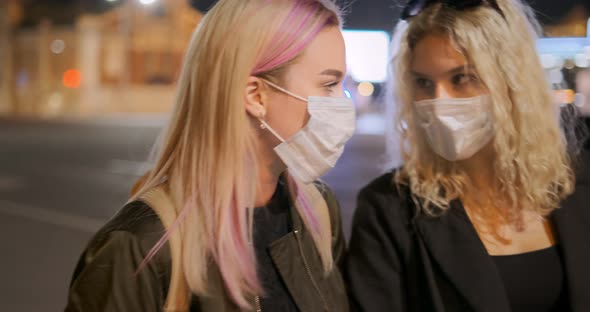 Ladies in Masks Walk Arm in Arm Along Night City Street