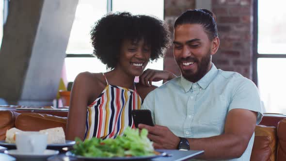 Diverse male and female colleagues sitting in cafe using a samrtphone having a discussion