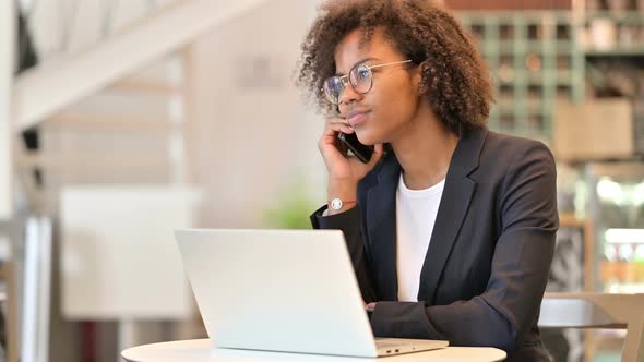 African Businesswoman with Laptop Talking on Smartphone at Cafe 