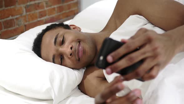 African Man in Bed Browsing Internet on Smartphone