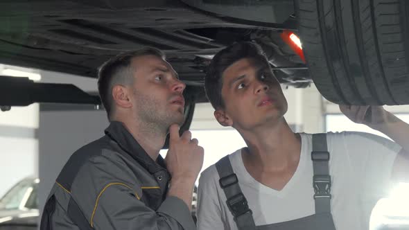 Two Auto Mechanics Checking Suspension of a Lifted Car at the Garage