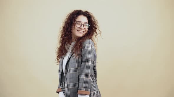 Portrait of a Young Woman with Curly Hair in a Gray Jacket and White Shirt with Glasses Posing