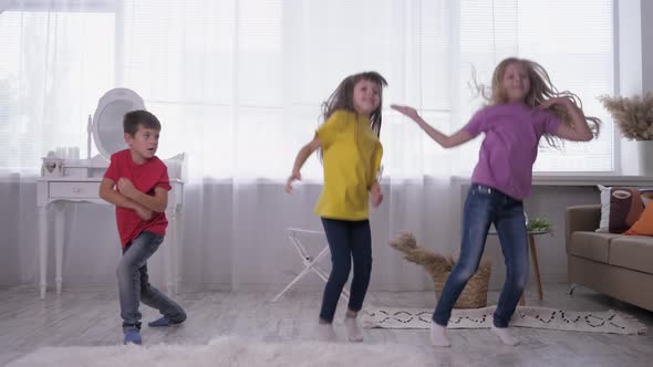 Children Dance and Jump in Multi Colored T-shirts Against a Bright Window in a White Room During