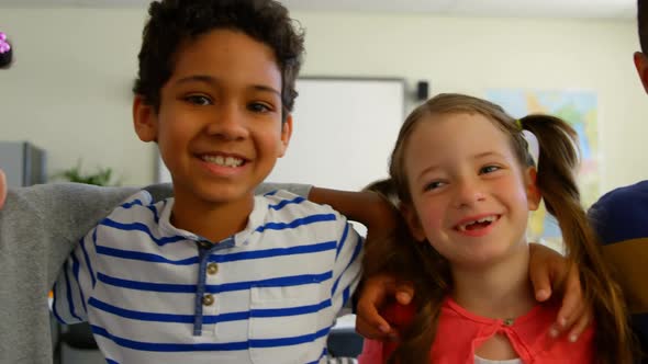 Front view of happy multi-ethnic schoolkids with arm around standing in classroom at school 4k