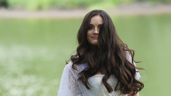 The Girl Looks Into the Camera and Revolves Around Her. Smile Model Against the Water.