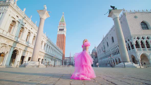 Girl with pink dress walks in the square in front of the bell tower in Venice