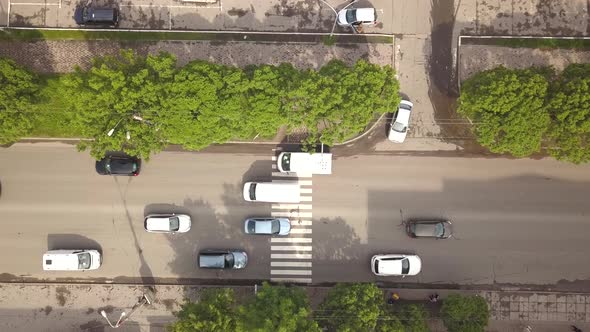 Top down aerial view of street with moving cars and zebra crosswalk with crossing pedestrians