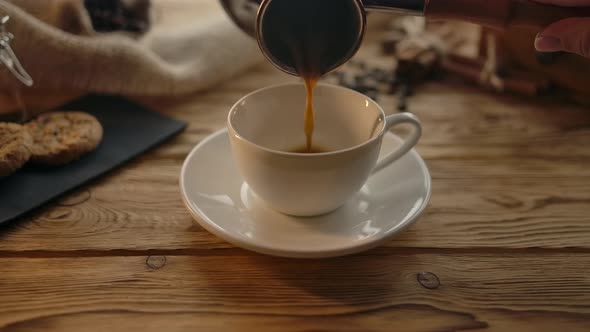 Pouring Coffee From the Cezve Into a Cup on a Wooden Table