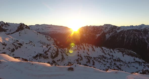 Alps sunrise at Chamrousse peaks in France with bright sun above ridge, Aerial orbit right