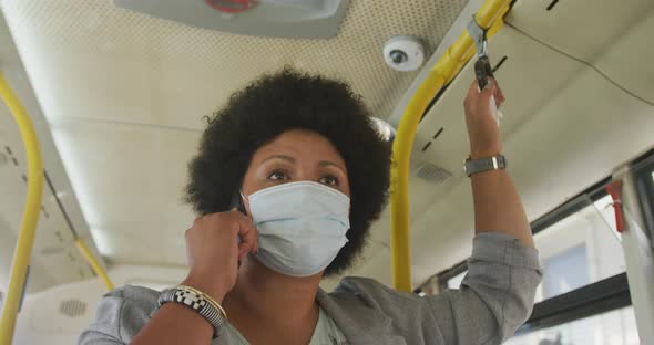 Plus size biracial woman wearing face mask talking on smartphone in bus