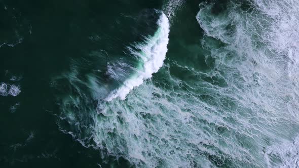 Moody ocean textures created by powerful crashing waves; drone descent