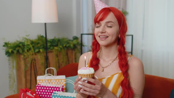 Happy Redhead Girl Celebrating Birthday Party Makes Wish Blowing Burning Candle on Small Cupcake